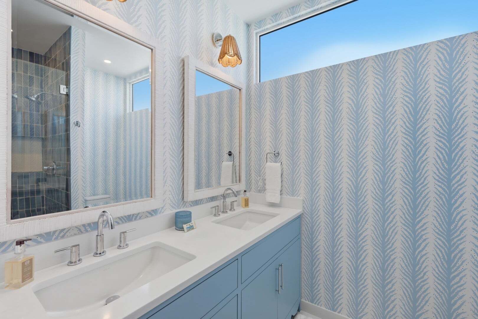 Een badkamer met twee wastafels, een grote spiegel, een handdoekhouder en behang met een patroon.