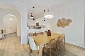 Eine moderne Küche mit weißen Schränken, einer zentralen Kochinsel und einem Essbereich mit Holztisch und Korbstühlen.