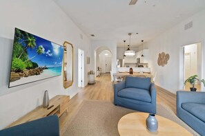 Een moderne woonkamer met een groot schilderij, een bank, een salontafel en een keuken op de achtergrond.