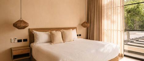 A bedroom with a large bed, two bedside tables, a hanging light fixture, and a view of greenery through the window.