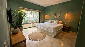 Ein Schlafzimmer mit Bett, Fernseher, Pflanze, Hängematte und Blick ins Freie.