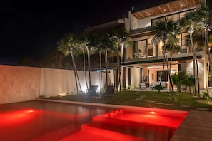 Una casa moderna de dos pisos amb piscina, mobiliari exterior i palmeres.