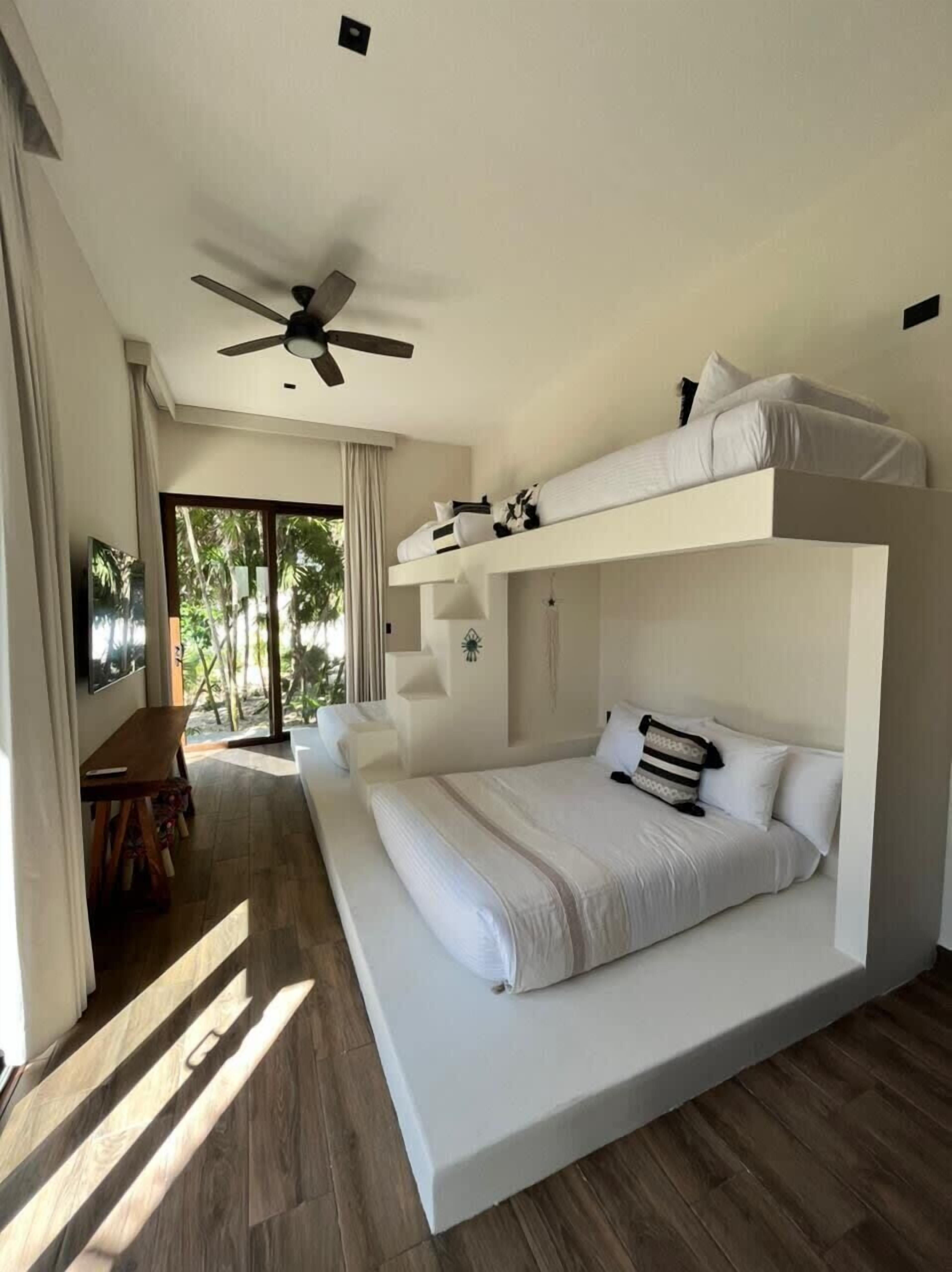 A modern bedroom with a bunk bed, a ceiling fan, and a view of the outdoors.