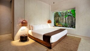 Et moderne soveværelse med en stor seng, et sengebord, en hængende lampe og et vindue med udsigt til grøn vegetation.