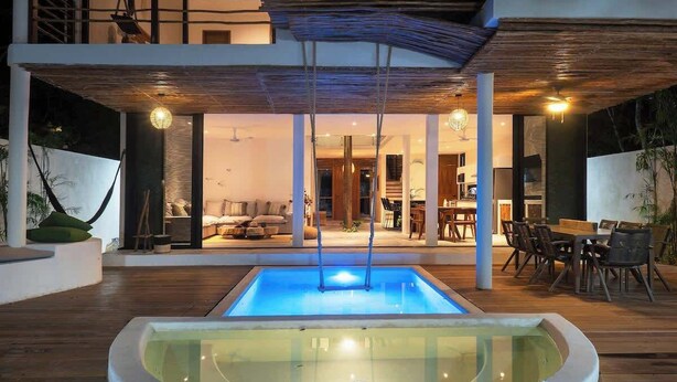Ein moderner, überdachter Innenpool mit Glasfassade, Holzboden und einem Essbereich mit Stühlen und Tischen.