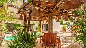 A covered outdoor area with a pool, wooden furniture, and hanging wicker lamps. - Casa Veleta: Designer Villa with Pool & Jacuzzi (Tulum)