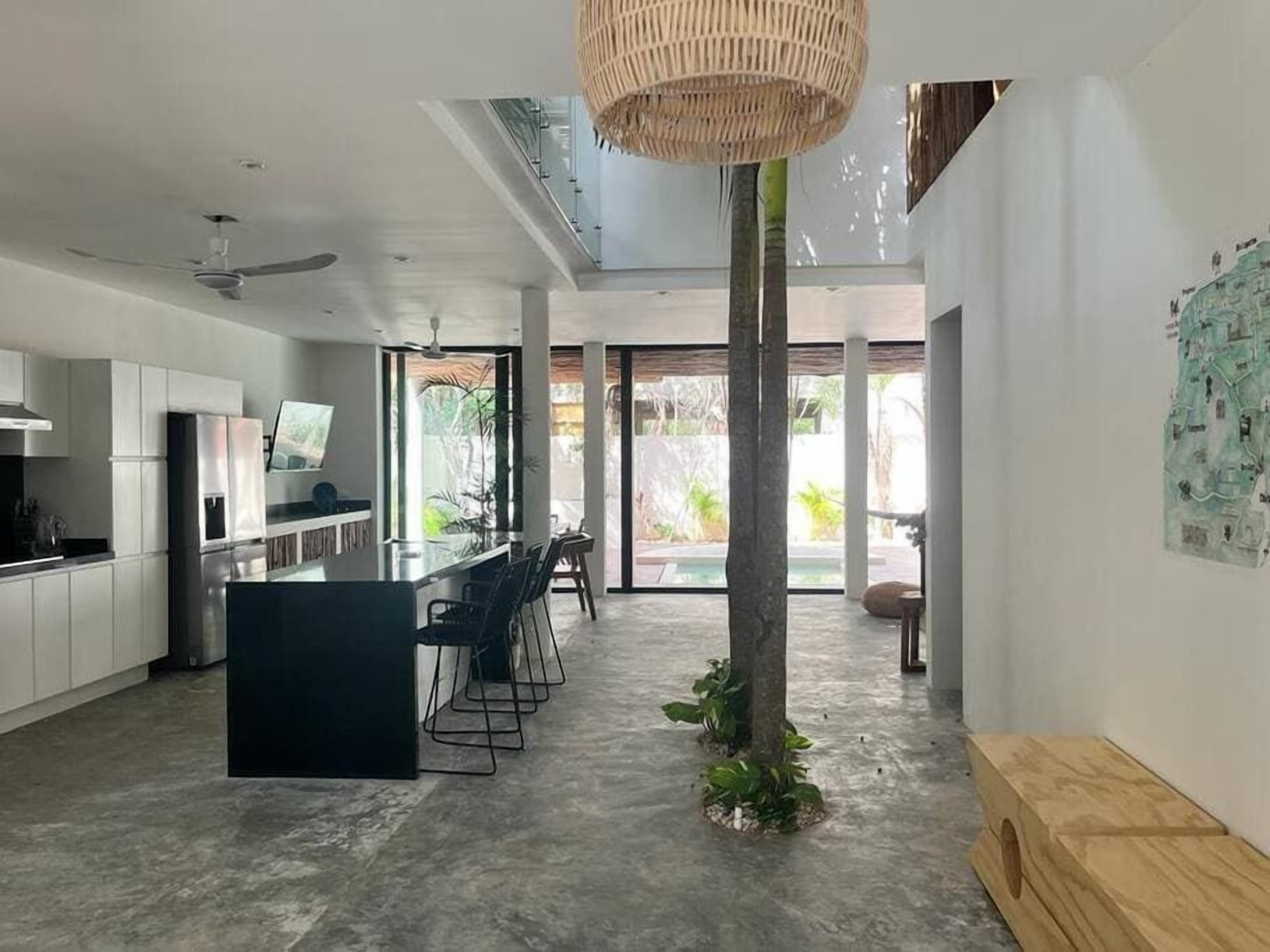 A modern kitchen with a central island, a dining area with chairs, and a large window.