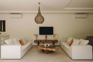 Un soggiorno con due divani bianchi, un tavolino in legno, una lampada a sospensione, una televisione a schermo piatto e un elegante consolle decorativa.