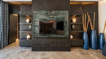 A modern living room with a large flat-screen TV mounted on a dark wall with a marble-like texture. There are shelves with decorative items and vases on the right side.