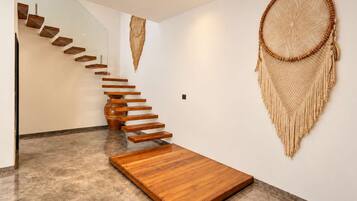 Un interno moderno con una scala in legno che conduce ad una piattaforma, un grande dreamcatcher intrecciato appeso al muro e un pavimento in marmo.