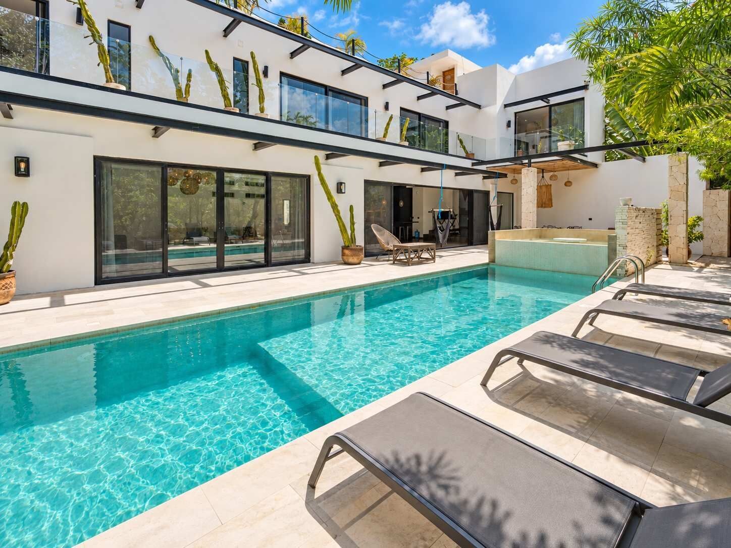 A modern poolside area with a clear pool, lounge chairs, and potted plants.
