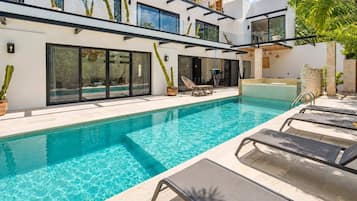 A modern poolside area with a clear pool, lounge chairs, and potted plants.
