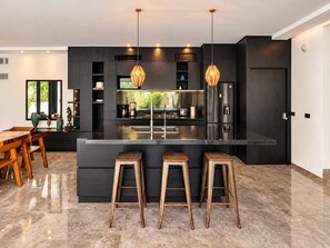 A modern kitchen with a central island, bar stools, and pendant lighting. - Renovated Modern Villa · 4BR · Huge Pool · Gated (Tulum)