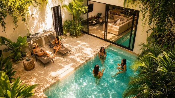 An indoor swimming pool with lounge chairs and a seating area, surrounded by greenery. - Villa con Limpieza Concierge y  Jacuzzi (Tulum)