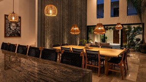 A dining area with a wooden table and chairs, pendant lights, and a large vertical textured wall. - Villa con Limpieza Concierge y  Jacuzzi (Tulum)