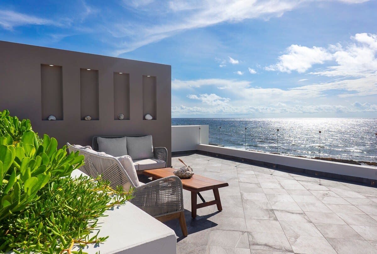 A rooftop terrace with a seating area, a view of the sea, and a modern wall with recessed lighting.