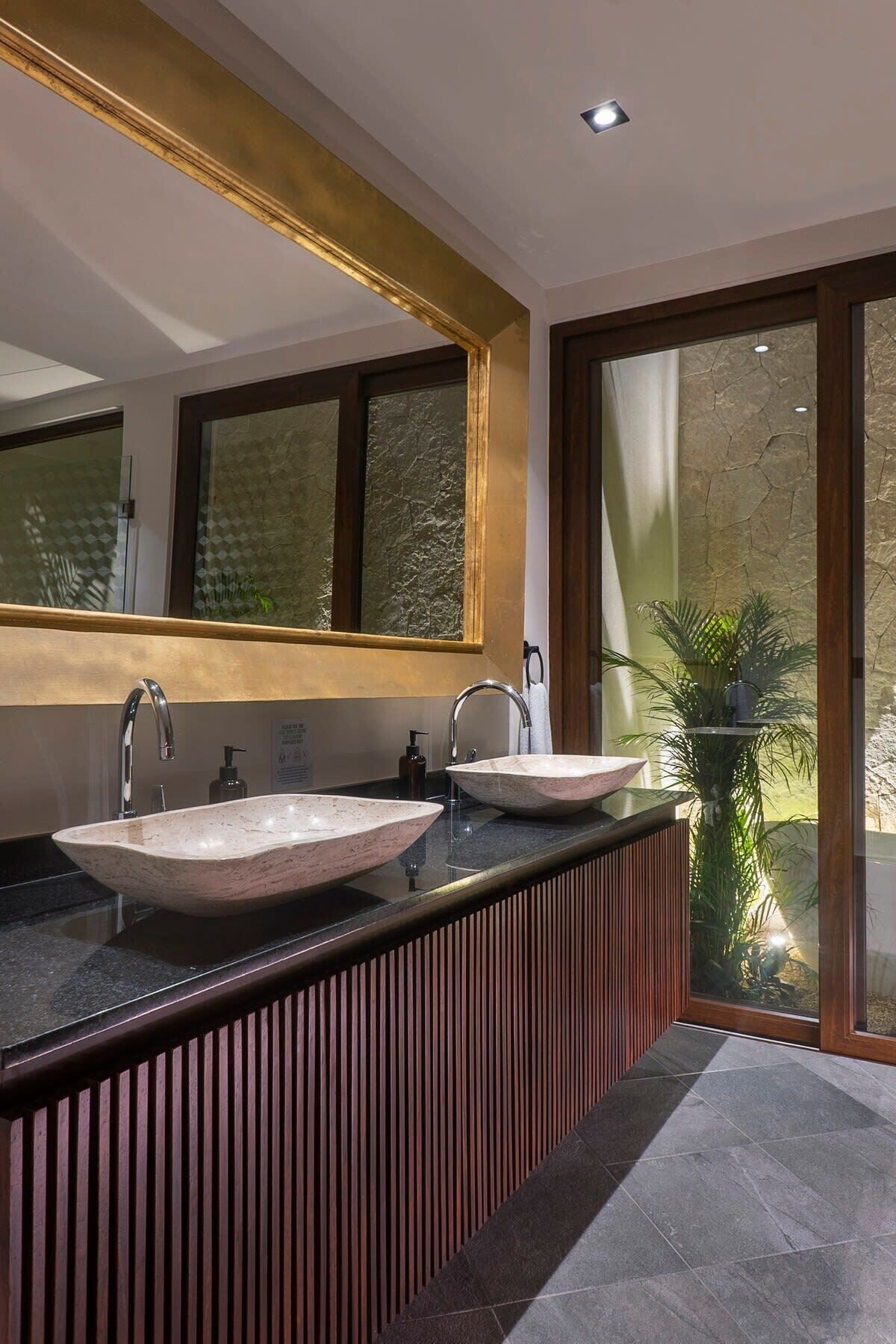 A modern bathroom with two vessel sinks, a large mirror, and a view of a balcony with plants.