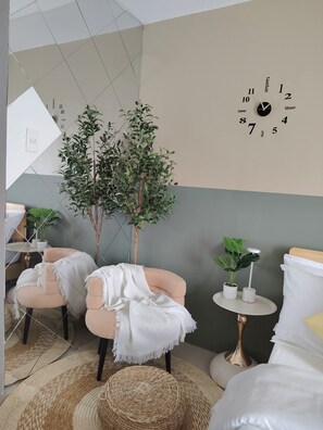 Ein modernes Zimmer mit einer Uhr an der Wand, zwei Stühlen, einem kleinen Tisch mit einer Pflanze und einem gewebten Korb am Boden.