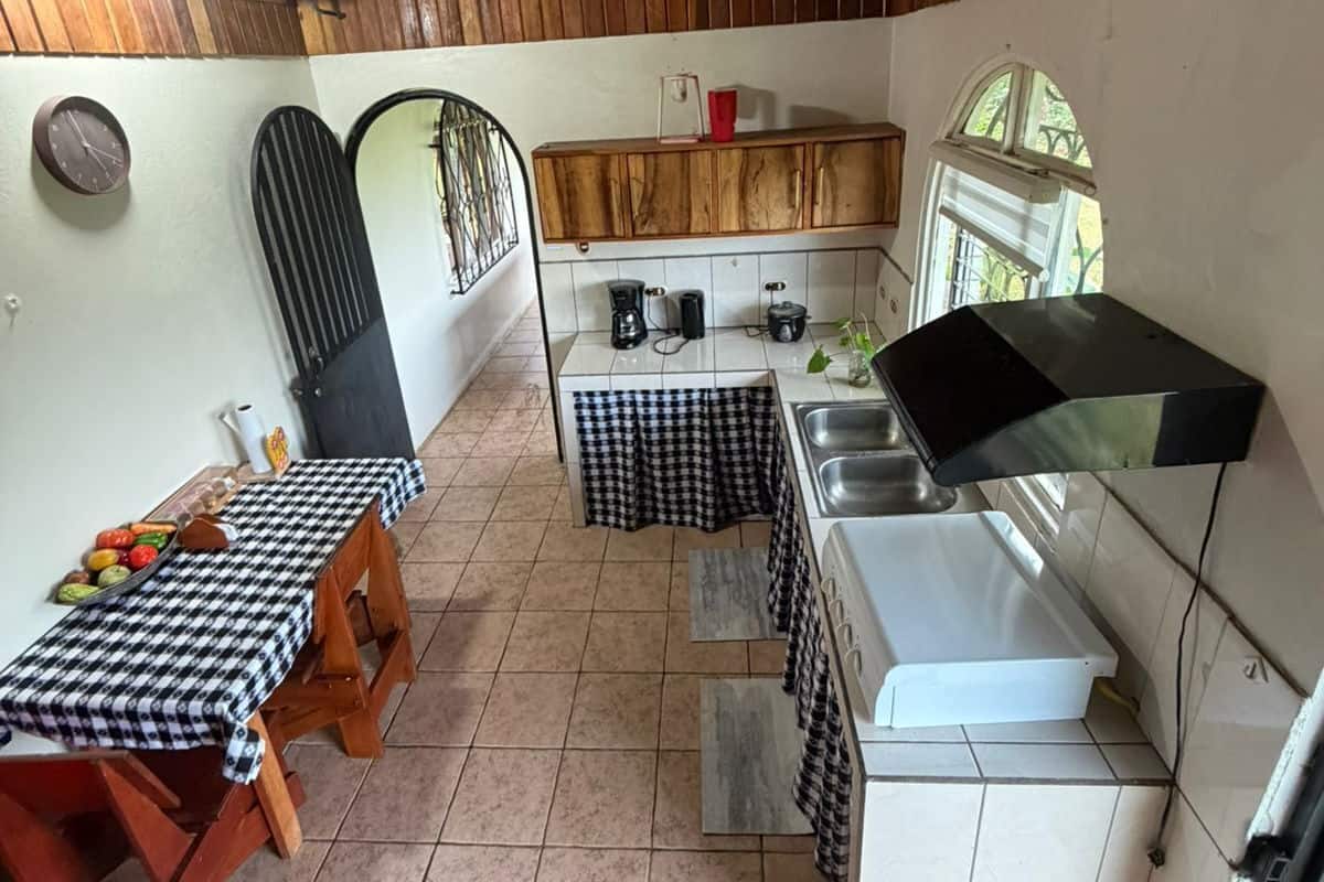 A compact kitchen with wooden cabinets, a sink, a coffee maker, and a table with a checkered tablecloth.