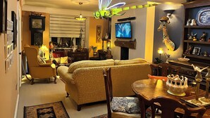 Ein Wohnzimmer mit einer Couch, Sesseln, einem Esstisch, Dekoration und einem Fernseher.
