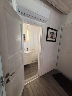 A hallway with a wooden floor, a white door, a framed picture on the wall, and an air conditioning unit above. - Bright summer house only 300 m from the water (Sjællands Odde)
