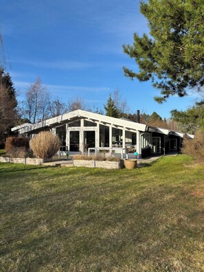 Een modern huis met een ruime veranda, omringd door een gazon en bomen.