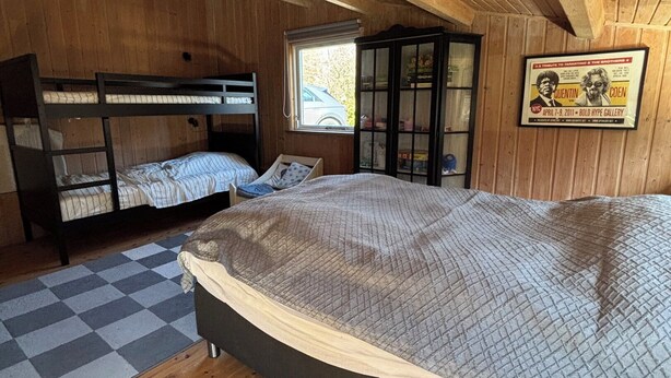 A wooden cabin room with bunk beds, a window, a cabinet, and a poster on the wall.