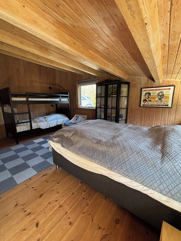 A wooden cabin room with bunk beds, a window, a cabinet, and a poster on the wall.