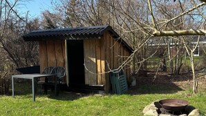 A rustic wooden shed with a metal door, a metal table, and a metal chair outside.