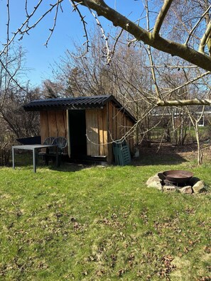 A rustic wooden shed with a metal door, a metal table, and a metal chair outside.