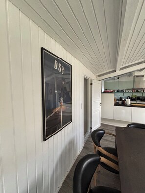 A dining area with a framed poster on the wall, a table with chairs, and a kitchen in the background.