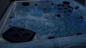 Un jacuzzi avec jets, entouré d’une clôture, et une maison en arrière-plan.
