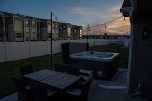 A patio area with a hot tub, outdoor seating, and string lights. - Stylish 4BR Hot Tub Retreat +Near Omaha + Garage + EV (Waterloo)