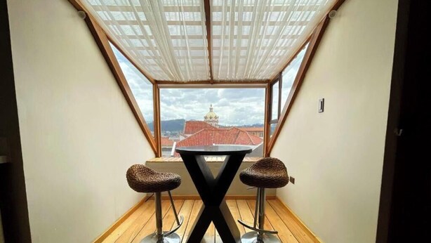 A small room with a table and two stools, a window with a view of a building with a dome, and a ceiling with a translucent fabric. - Hotel Ensueños by HHG (Cuenca)