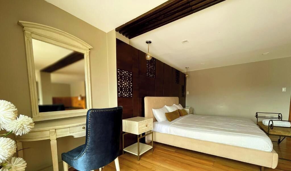 A bedroom with a bed, a desk, a chair, a dresser, and a large mirror.