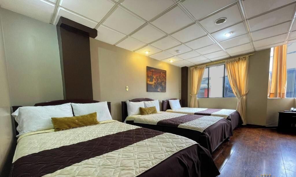 A hotel room with three beds, a painting on the wall, and a window with curtains.