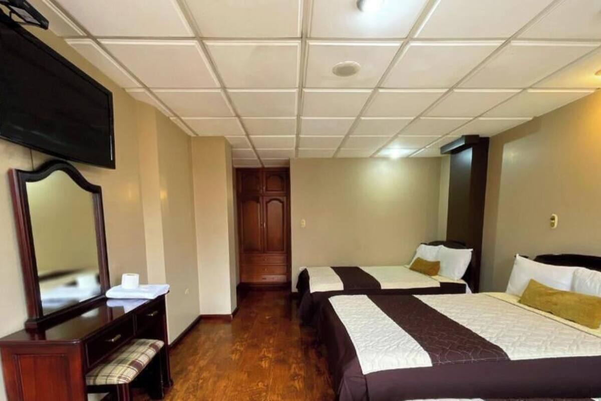 A hotel room with two beds, a TV, a mirror, and a wooden floor.