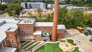 Un edificio grande de ladrillo con una chimenea destacada, un estacionamiento y un césped bien cuidado.