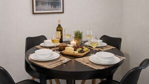 Una mesa redonda para comer con platos blancos, copas y una botella de vino blanco. En el centro, hay queso, uvas y una vela.