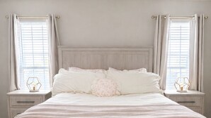 A bedroom with a large bed, two bedside tables, and a window with curtains. - The Rally Point @ Antietam (Columbus)