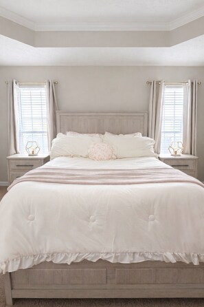 A bedroom with a large bed, two bedside tables, and a window with curtains. - The Rally Point @ Antietam (Columbus)