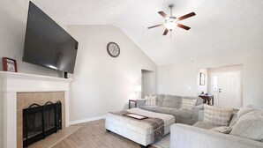 A living room with a fireplace, a flat-screen TV, a ceiling fan, and a sofa. - The Rally Point @ Antietam (Columbus)