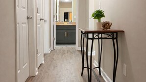 A hallway with white doors, a wooden floor, a small table with a plant, and a mirror on the wall. - The Rally Point @ Antietam (Columbus)