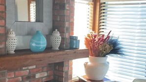 Ein Zimmer mit Kamin aus Backsteinen, einem Spiegel und einem Fenster mit Jalousien.