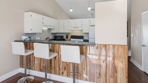 Una cocina con armarios blancos, una isla de madera con taburetes de bar, un microondas y una estufa.