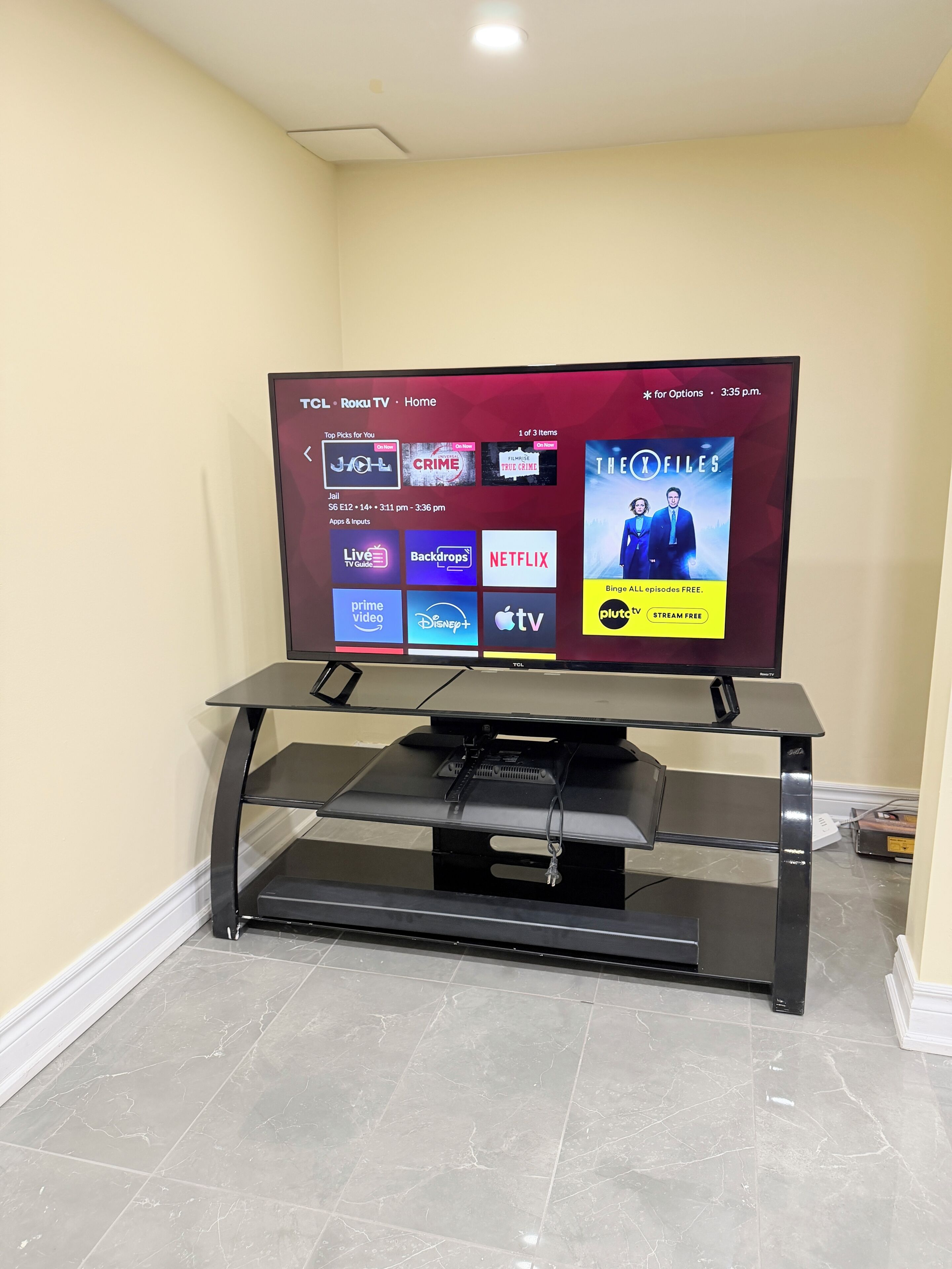 Een flatscreen-tv bevestigd aan een zwart tv-meubel met een voet, waarop een streamingdienstinterface met diverse inhoudsopties wordt getoond.