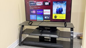 Un téléviseur à écran plat fixé sur un meuble de télévision noir doté d’un support, affichant l’interface d’un service de diffusion en continu proposant différentes options de contenu.