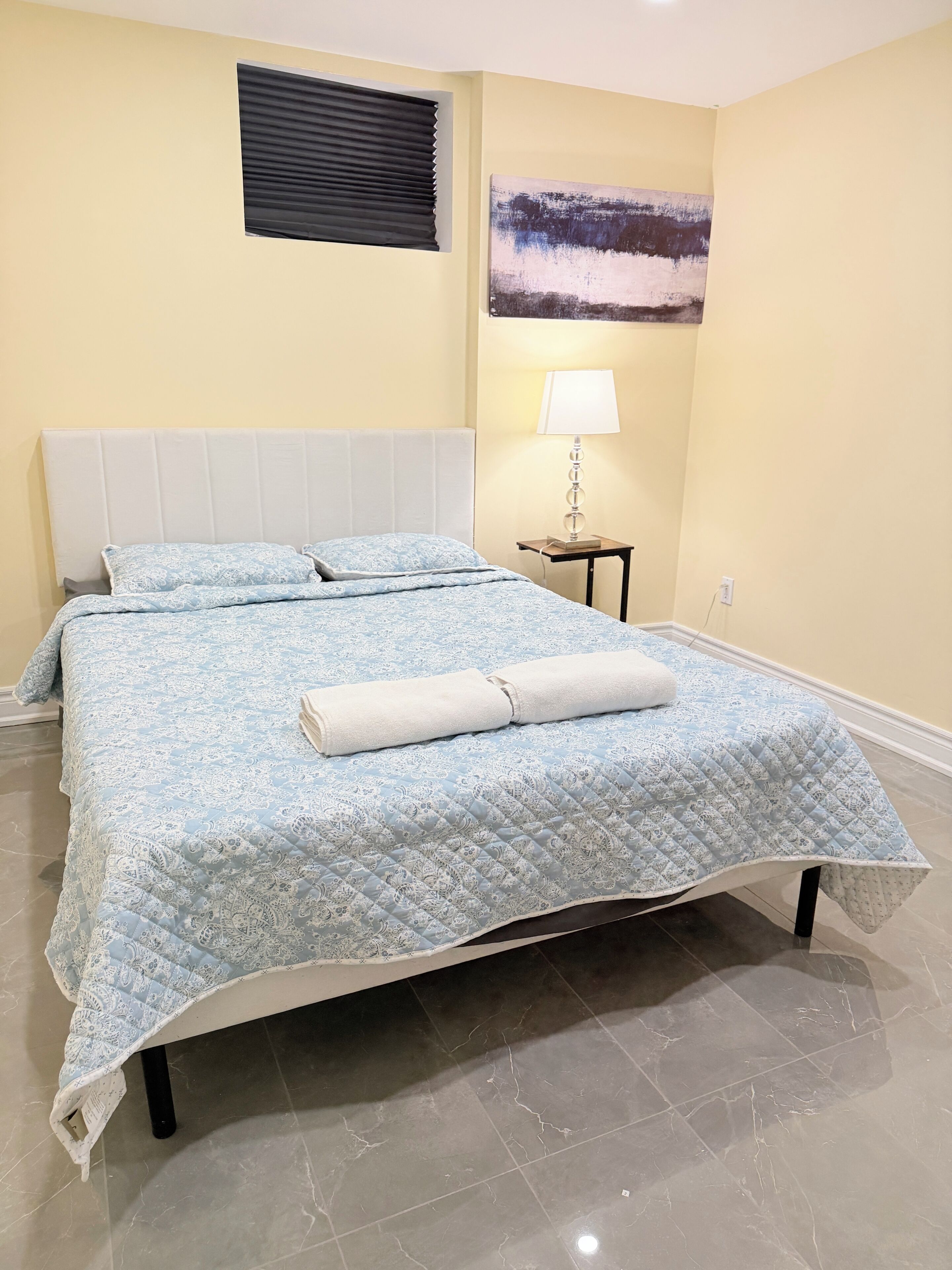 A bed with a quilted headboard, a bedside lamp, and a painting on the wall.
