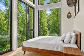 Ein Schlafzimmer mit großem Fenster, einem Holzbettgestell und einem Nachttisch.