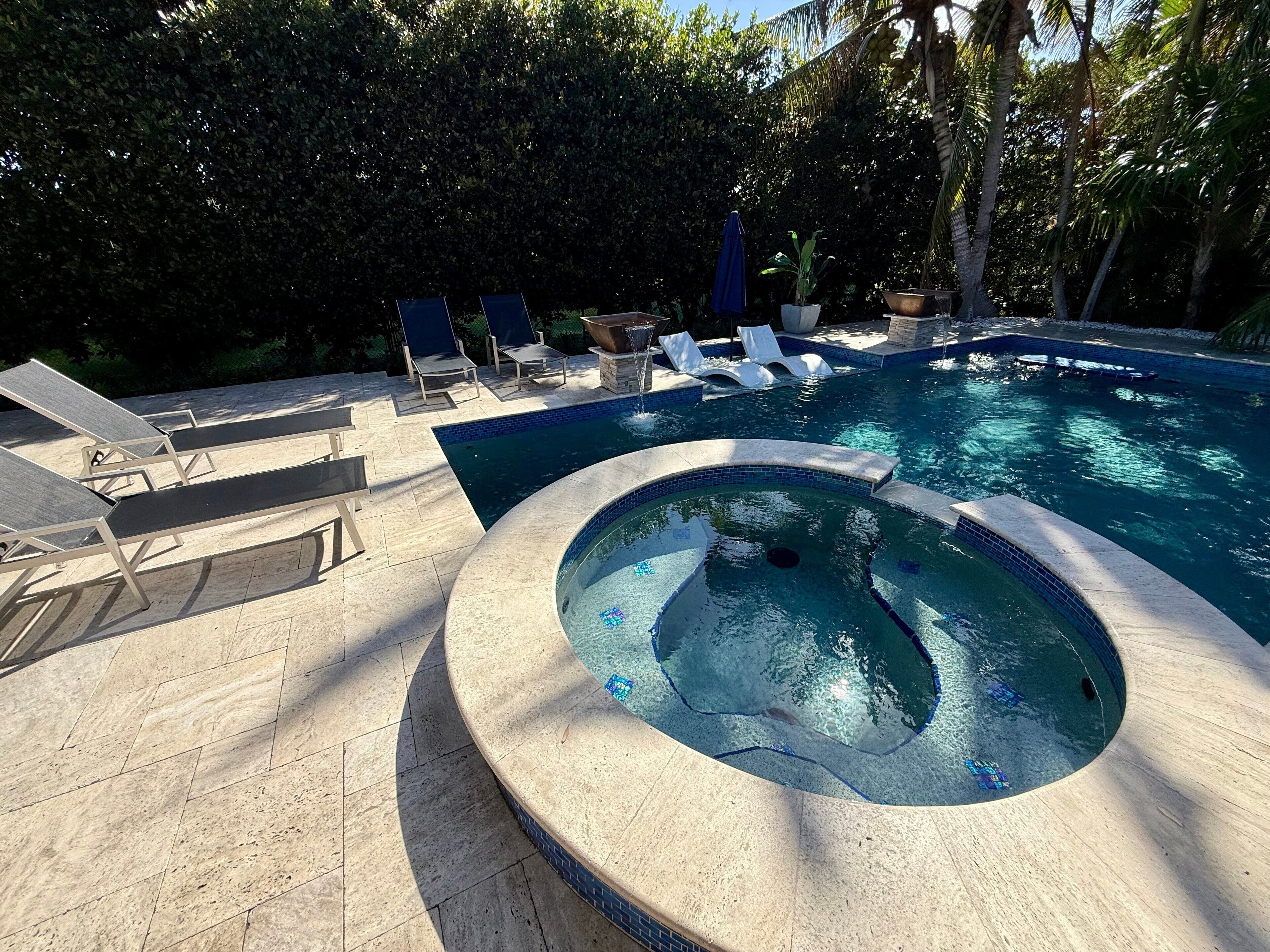 A swimming pool with lounge chairs and a hot tub.